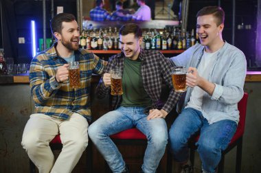 Friends having fun. Happy young men in casual wear drinking beer in pub