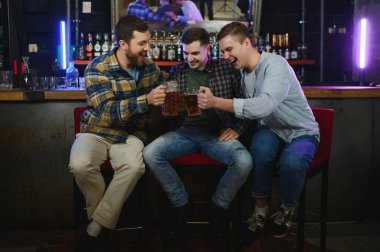 Friends having fun. Happy young men in casual wear drinking beer in pub