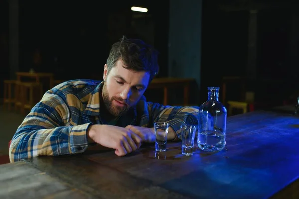 It was a hard day. Depressed young man drinking vodka in bar.