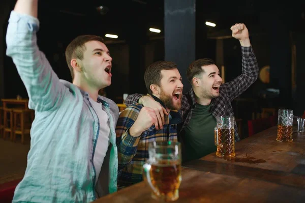 Soccer fans cheering for favourite team while enjoying drinks. Group of supporters celebrating victory while watching football match on tv in a club. Happy friends shouting while cheering for a goal