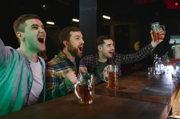 Sport, people, leisure, friendship, entertainment concept - happy male football fans or good yuong friends drinking beer, celebrating victory at bar or pub. Human positive emotions concept.