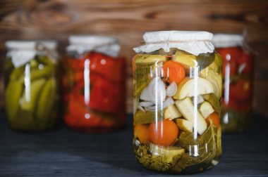Canned cucumbers and tomatoes with craft lids on a wooden background. Cucumbers and tomatoes with place for text. Stocks of canned food. Harvest, stocks for the winter