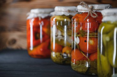 Canned cucumbers and tomatoes with craft lids on a wooden background. Cucumbers and tomatoes with place for text. Stocks of canned food. Harvest, stocks for the winter