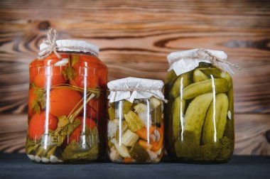 Canned cucumbers and tomatoes with craft lids on a wooden background. Cucumbers and tomatoes with place for text. Stocks of canned food. Harvest, stocks for the winter