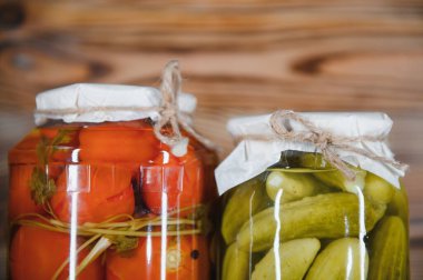 Canned cucumbers and tomatoes with craft lids on a wooden background. Cucumbers and tomatoes with place for text. Stocks of canned food. Harvest, stocks for the winter