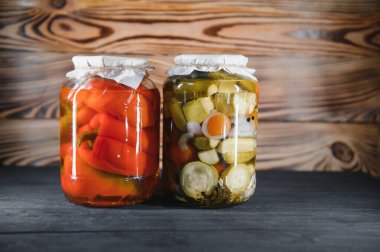 Canned cucumbers and tomatoes with craft lids on a wooden background. Cucumbers and tomatoes with place for text. Stocks of canned food. Harvest, stocks for the winter