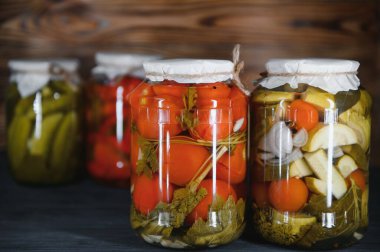 Canned cucumbers and tomatoes with craft lids on a wooden background. Cucumbers and tomatoes with place for text. Stocks of canned food. Harvest, stocks for the winter