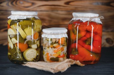 Canned cucumbers and tomatoes with craft lids on a wooden background. Cucumbers and tomatoes with place for text. Stocks of canned food. Harvest, stocks for the winter