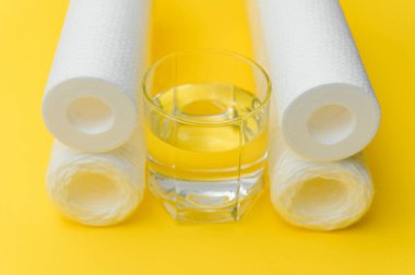 Su filtreleri. Karbon kartuşlar ve sarı arka planda bir bardak. Ev filtreleme sistemi.