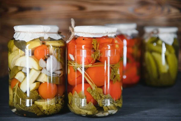 Jars of pickled vegetables on rustic wooden background.