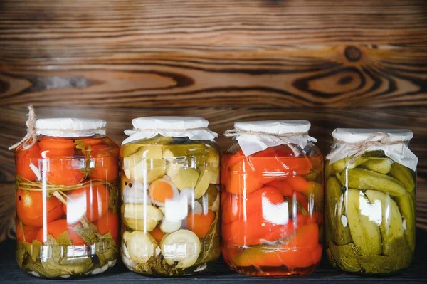 Jars of pickled vegetables on rustic wooden background.