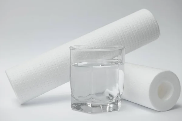 Water filters. Carbon cartridges and a glass on a yellow background. Household filtration system.