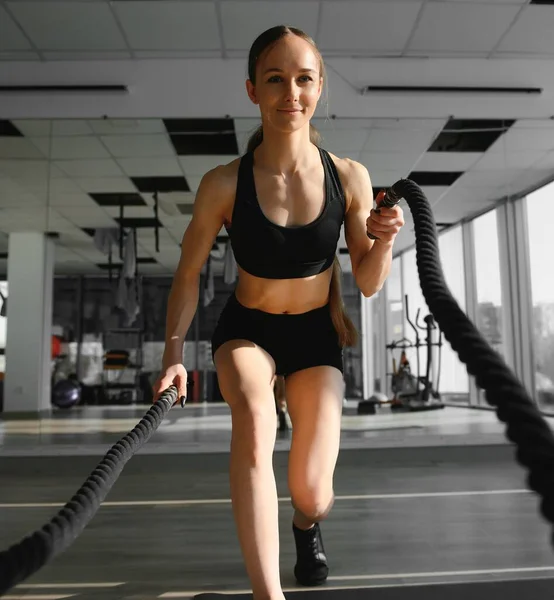 Woman training with battle ropes in gym.
