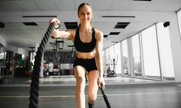 Athletic Female in a Gym Exercises with Battle Ropes During Her Fitness Workout High-Intensity Interval Training. She\'s Muscular and Sweaty.