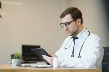 male doctor using tablet computer at his office. General practitioner using digital tablet at his clinic