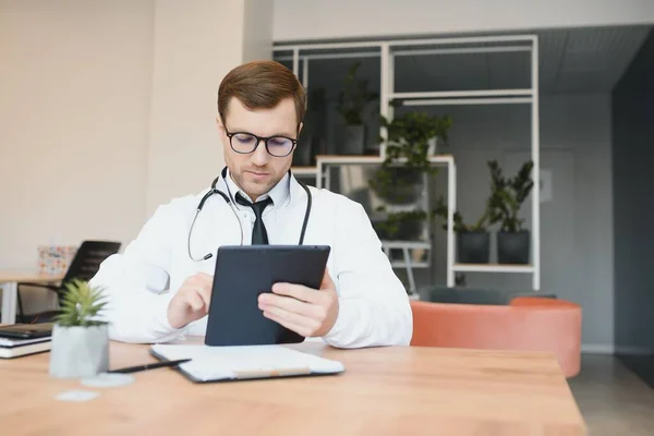 male doctor using tablet computer at his office. General practitioner using digital tablet at his clinic