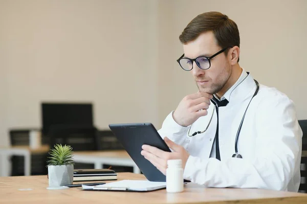 male doctor using tablet computer at his office. General practitioner using digital tablet at his clinic