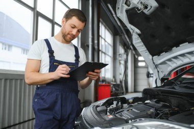car mechanic writing while holding clipboard near cars.