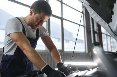 Özel üniformalı, el feneri tutan, kaputun altında araba tamirhanesinde tamirat yapan yakışıklı bir erkek tamirci..