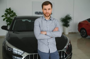 Final decision. Shot of a handsome young man standing in front of a new car at the dealership thinking rubbing his chin.