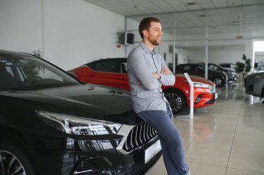 Final decision. Shot of a handsome young man standing in front of a new car at the dealership thinking rubbing his chin.