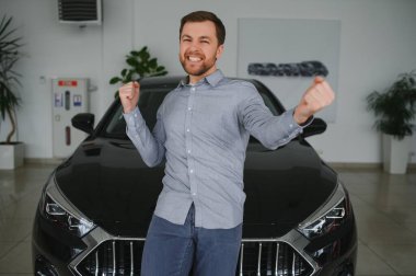 Araba galerisini ziyaret ediyorum. Yakışıklı sakallı adam yeni arabasını okşuyor ve gülümsüyor.