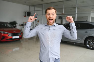 Emotional handsome guy raising hand up and smiling at camera. Rich man buying auto at luxury dealership salon.