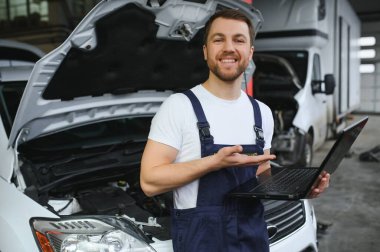 With laptop. Adult man in uniform works in the automobile salon