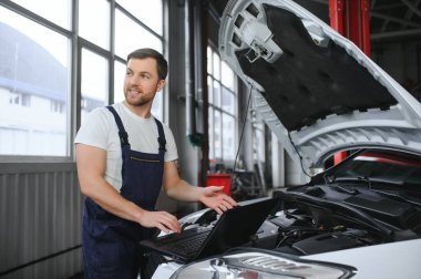 With laptop. Adult man in uniform works in the automobile salon
