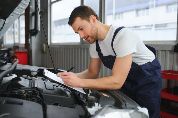car service, repair, maintenance and people concept - happy smiling auto mechanic man or smith with clipboard at workshop.