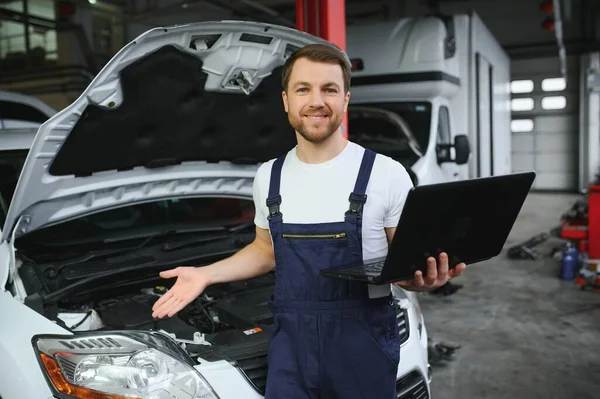 With laptop. Adult man in uniform works in the automobile salon