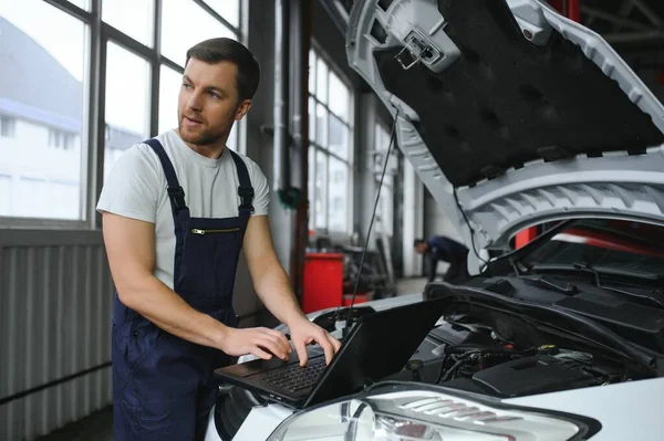 With laptop. Adult man in uniform works in the automobile salon