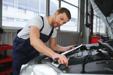 car mechanic writing while holding clipboard near cars.