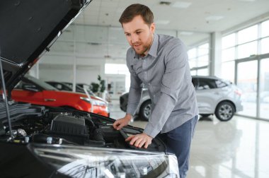 Araba galerisini ziyaret ediyorum. Yakışıklı sakallı adam yeni arabasını okşuyor ve gülümsüyor.