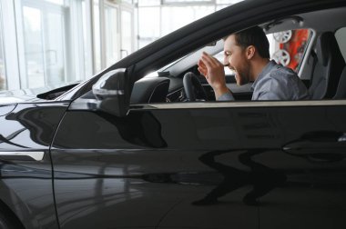 Yeni arabanın içindeki direksiyonda mutlu genç sürücü. Araba galerisinde yaşam tarzı sahnesi.