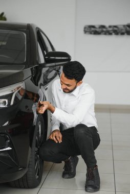 A young Indian man chooses a new car at a car dealership.