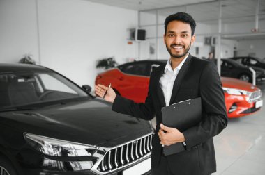 indian cheerful car salesman showing new car at showroom.