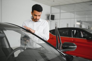 happy indian man checking car features at showroom.