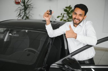 Smiling, friendly indian car seller standing in car salon
