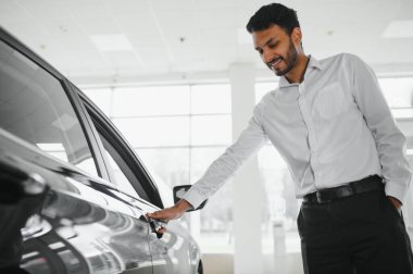 A young Indian man chooses a new car at a car dealership.