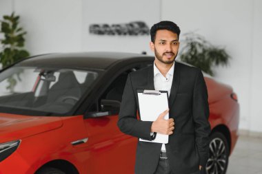 indian cheerful car salesman showing new car at showroom.