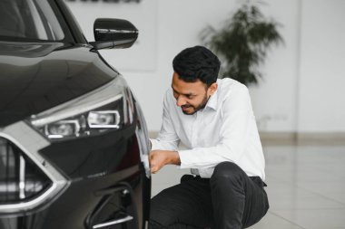 Indian man adult customer male buyer client wears classic suit white shirt chooses auto wants to buy new automobile touch check car in showroom vehicle salon dealership store motor show indoor. Sales concept.