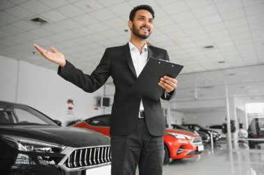 indian cheerful car salesman showing new car at showroom.