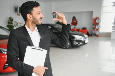 Smiling, friendly indian car seller standing in car salon