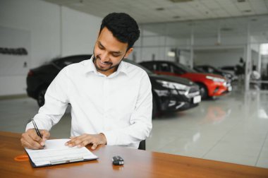 young indian man signing documents at car dealership.