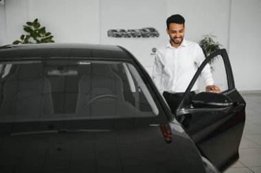 happy indian man checking car features at showroom.