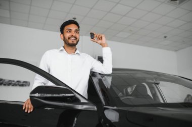 Smiling, friendly indian car seller standing in car salon