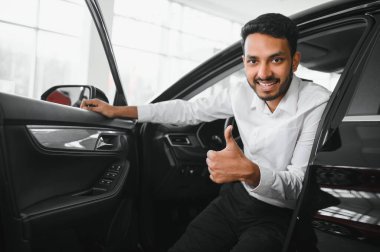 A young Indian man chooses a new car at a car dealership.