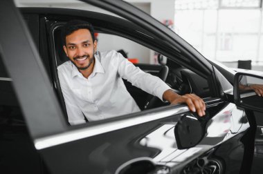 happy indian man checking car features at showroom.