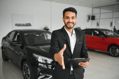 indian cheerful car salesman showing new car at showroom.